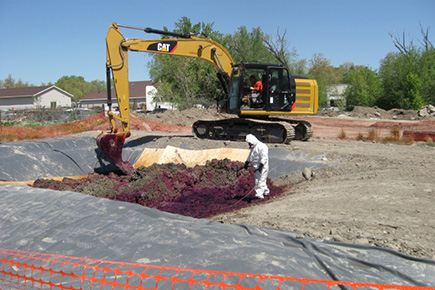 Contaminated soil being treated and cleaned by a person in a hazmat suit and a backhoe mixing the soil with the treatment solution.