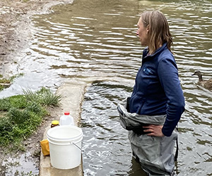 Woman with water quality testing equipment and wearing waders standing in the water