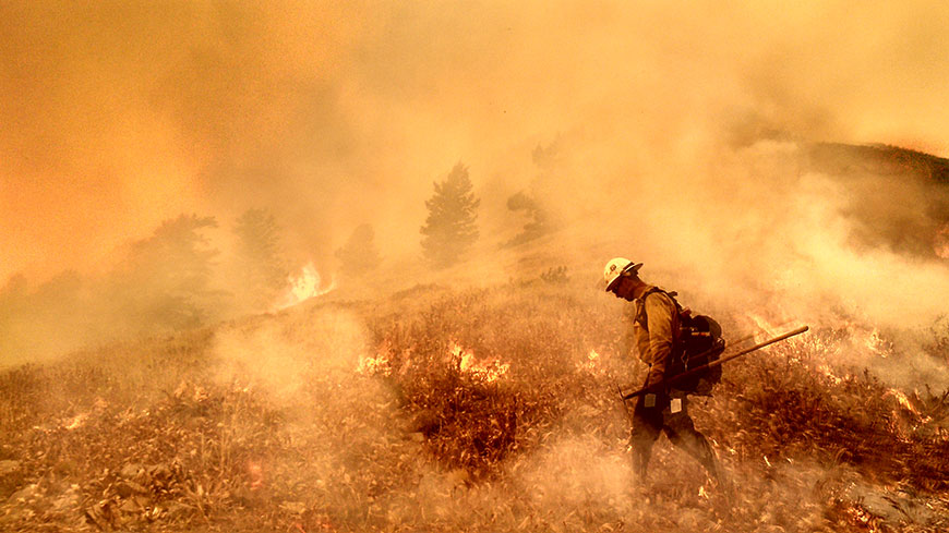 A wildland firefighter walks through a blaze in Utah.